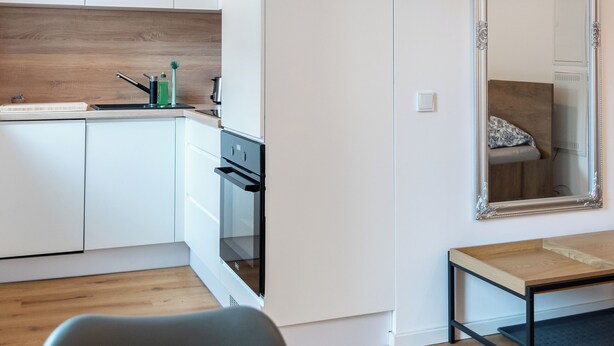 Een moderne keuken met witte kasten, een houten aanrecht en een grote spiegel.