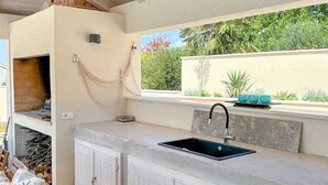 A kitchen with a built-in sink, wooden cabinets, a hanging light, and a view of greenery outside. - Villa Sea Whisper - location and charm by MyWaycation (Splitska)