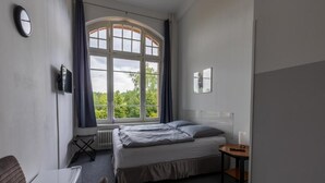 A bedroom with a bed, a desk, a chair, a window with curtains, and a radiator. - Motel Home Wittenau (Berlin)