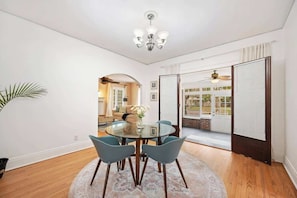 A dining area with a round glass table, four chairs, a chandelier, and a view of the backyard through a sliding door.