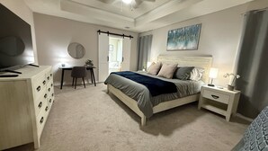 Ein Schlafzimmer mit einem Bett, einem Schreibtisch, einem Sessel, einem Fernseher, einem Deckenventilator und einem Bild an der Wand.