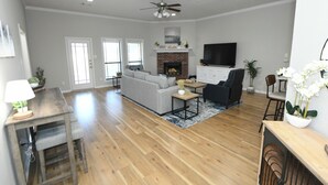 Ein geräumiges Wohnzimmer mit Holzböden, einem grauen Ecksofa, einem schwarzen Sessel, einem Couchtisch und einem Kamin.