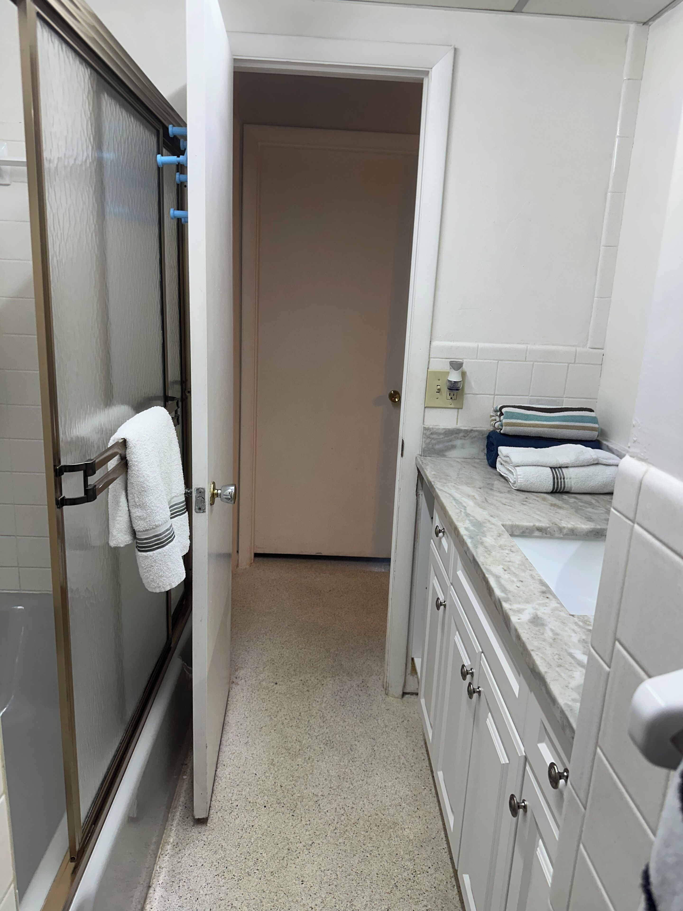 A narrow bathroom with a glass shower door, a white sink, and a countertop with towels.
