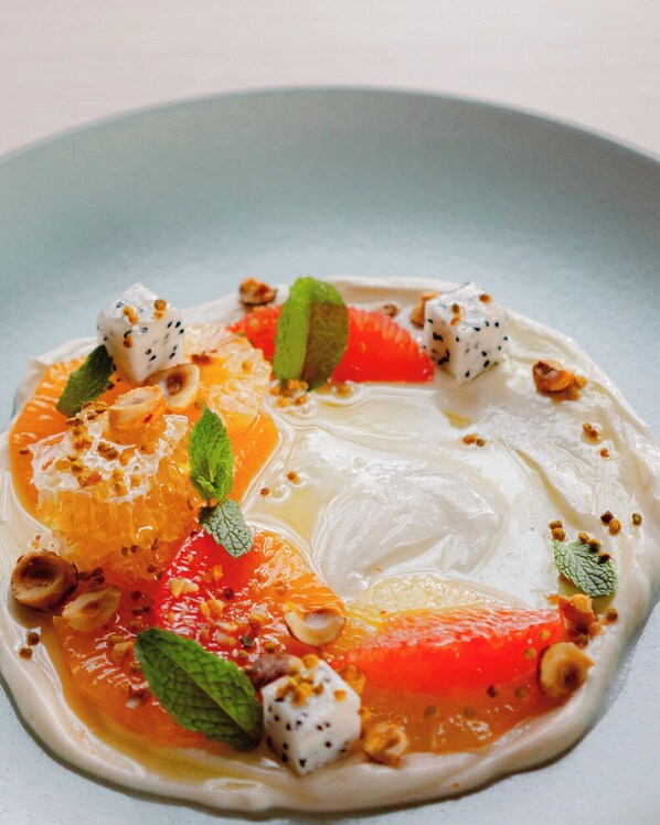 A dessert plate with a creamy white base, topped with orange slices, a green leaf, and small white and brown dots.