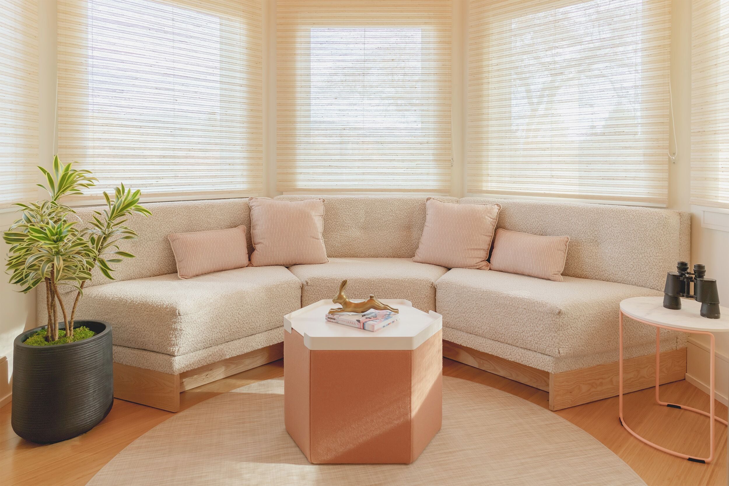 A corner living room with a beige sectional sofa, a round coffee table, a potted plant, and a small side table with binoculars.