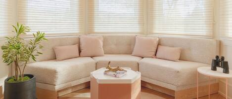 A corner living room with a beige sectional sofa, a round coffee table, a potted plant, and a small side table with binoculars.