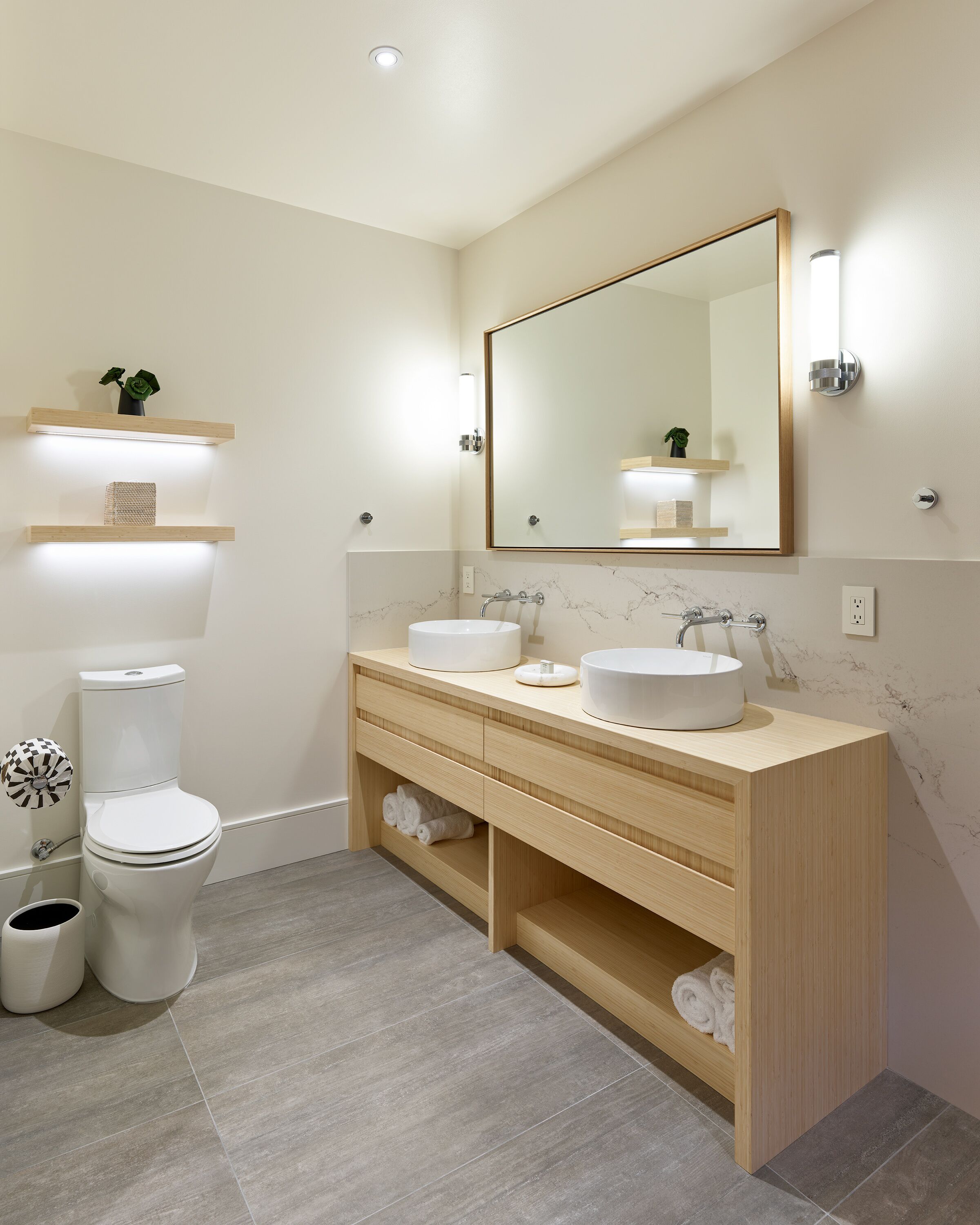 A modern bathroom with a toilet, two sinks, a mirror, and built-in shelves.