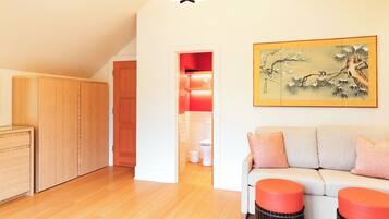 A room with a wooden wardrobe, a sofa with orange cushions, a painting on the wall, and a ceiling light fixture.