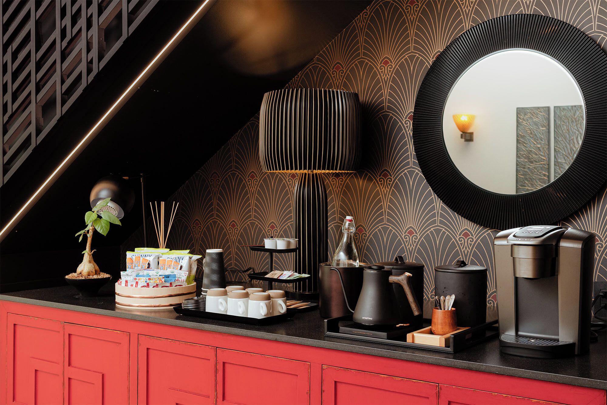 A modern kitchen with a red cabinet, a coffee maker, a kettle, and a mirror on the wall.