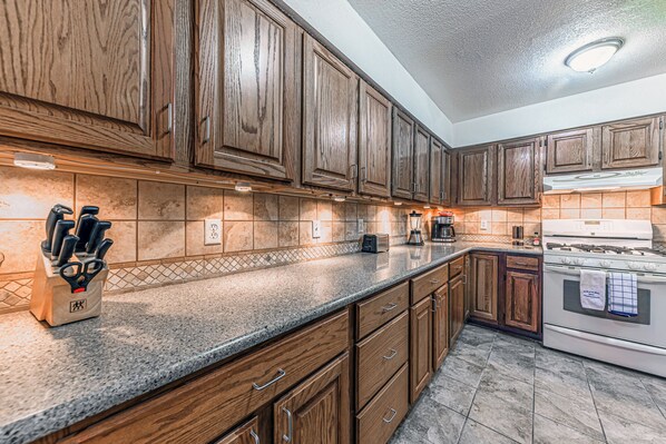 A kitchen with wooden cabinets, granite countertops, a stove, and a coffee maker. - North Street Escape (Ruidoso)
