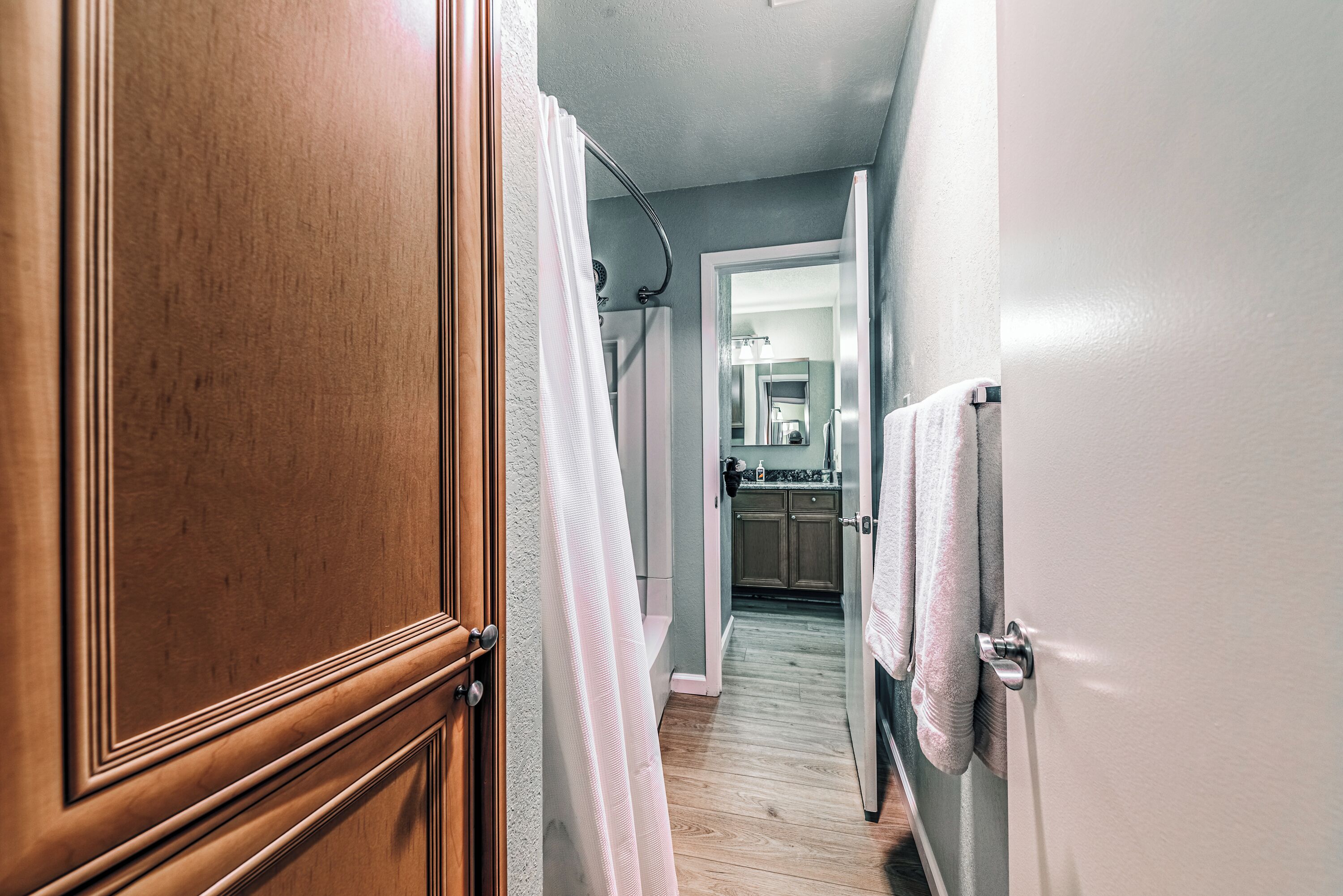 A hallway with wooden doors, a white towel hanging on a door, and a kitchen area visible in the background.