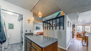 Een moderne keuken met granieten aanrechtbladen, houten kastjes en een centraal eiland. Er is een trap die leidt naar een hoger niveau, en een eethoek met houten stoelen.