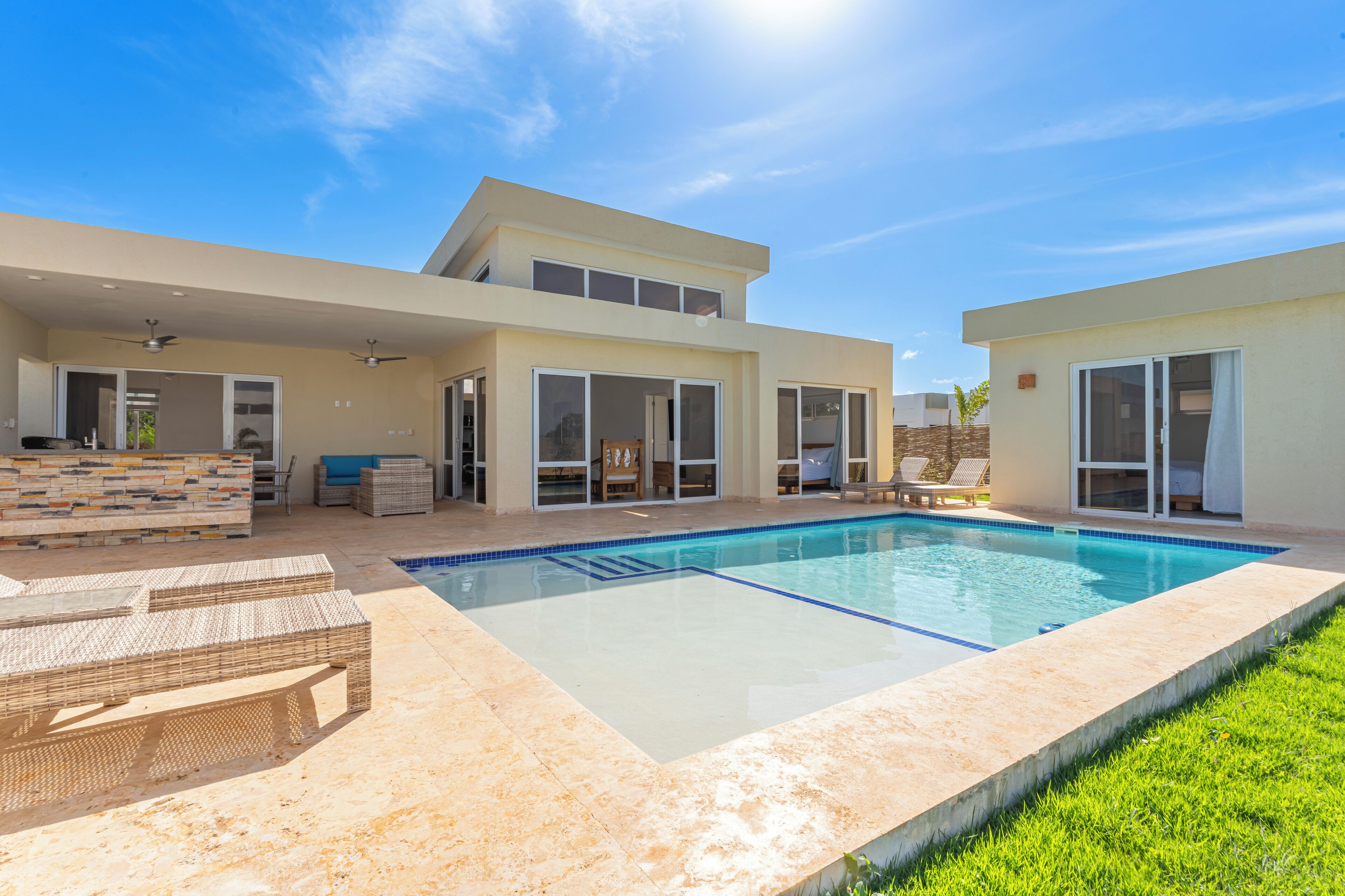 Una casa moderna de dos pisos con piscina, mobiliario exterior y puertas correderas de vidrio.