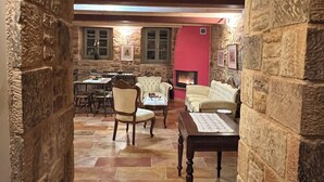 A stone-walled corridor leading to a living area with a fireplace, a dining table, and several chairs. - Pietra Rossa (Chios)