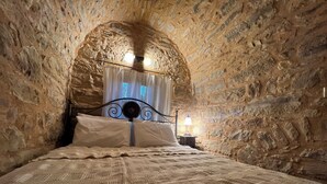 A stone-walled bedroom with a bed, a nightstand, and a lamp. - Pietra Rossa (Chios)