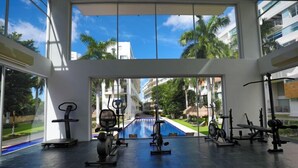 Ein Fitnessstudio mit unterschiedlichen Trainingsgeräten, großen Fenstern und Blick auf einen Pool sowie Gebäude.