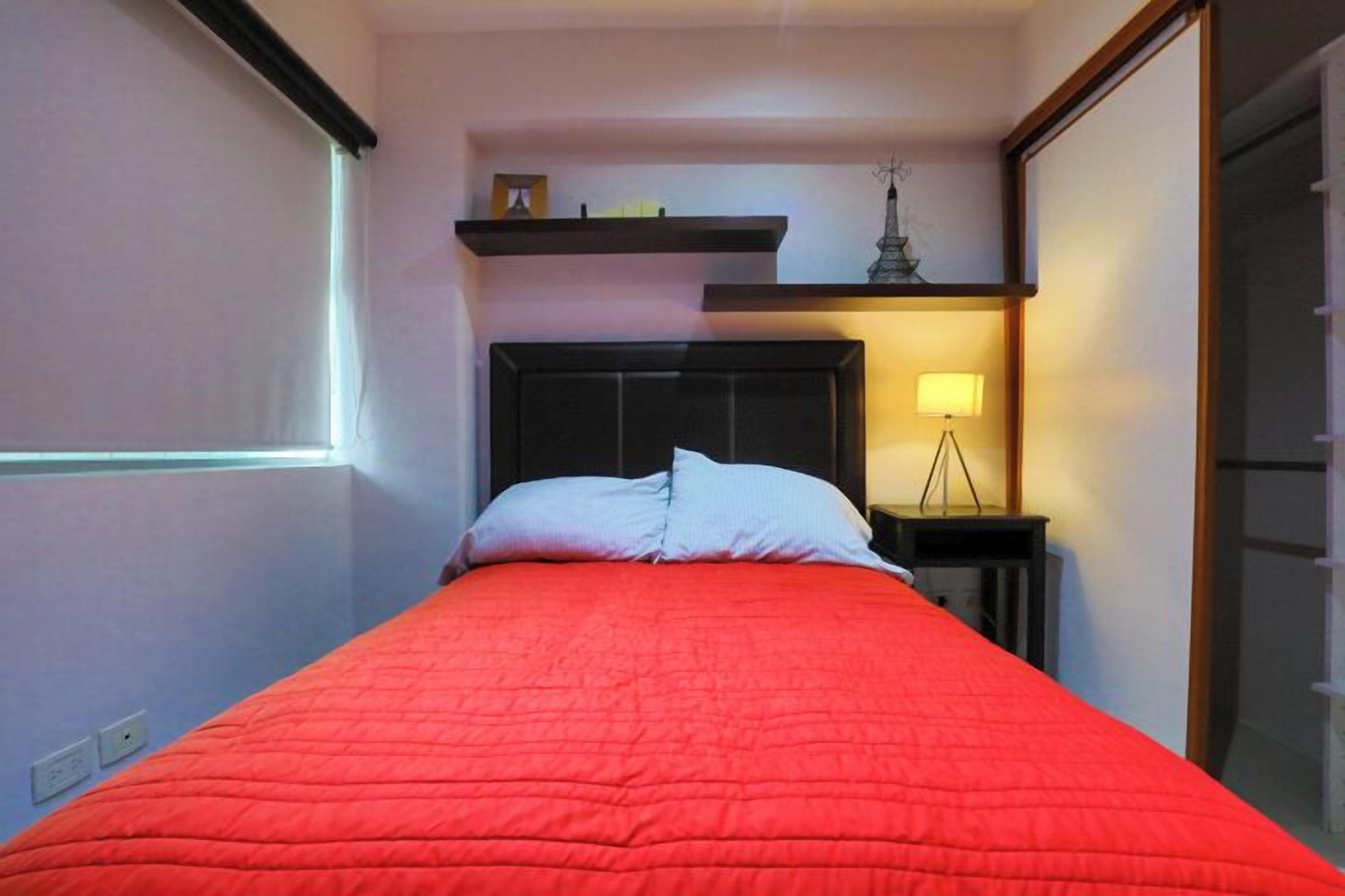 A room with a bed, a nightstand, a lamp, and a shelf with a decorative item.