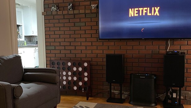 Una sala de estar con pared de ladrillo, un televisor de pantalla plana mostrando 'NETFLIX', dos altavoces, un sofá y una mesa de centro.