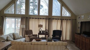 A spacious living room with high ceilings and large windows, featuring a sofa, two armchairs, a television, and a cabinet. - Cute House on Lake Hartwell- Dock Access!
PETS ALLOWED! (Townville)