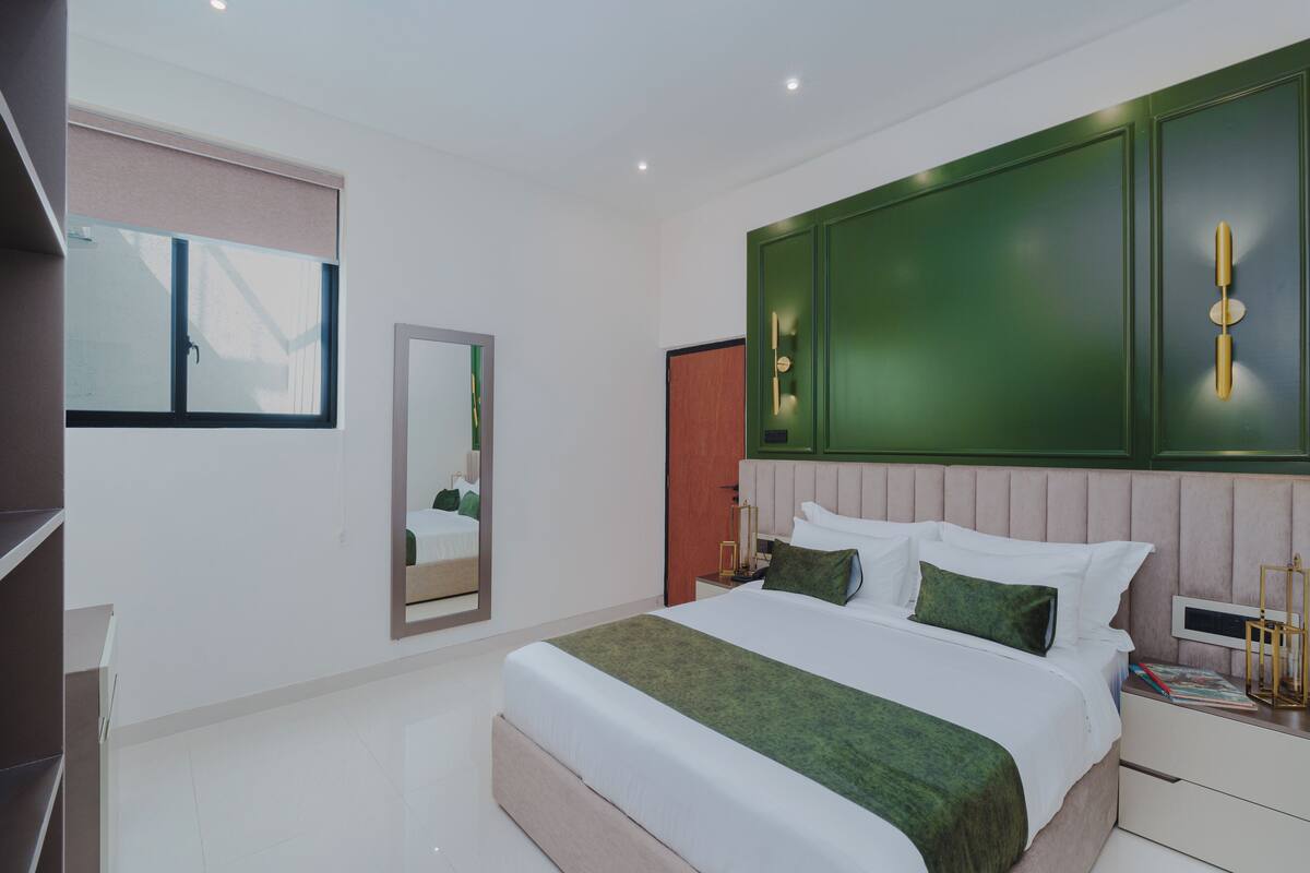 A modern bedroom with a large bed, a bedside table, a mirror, and green accent walls.