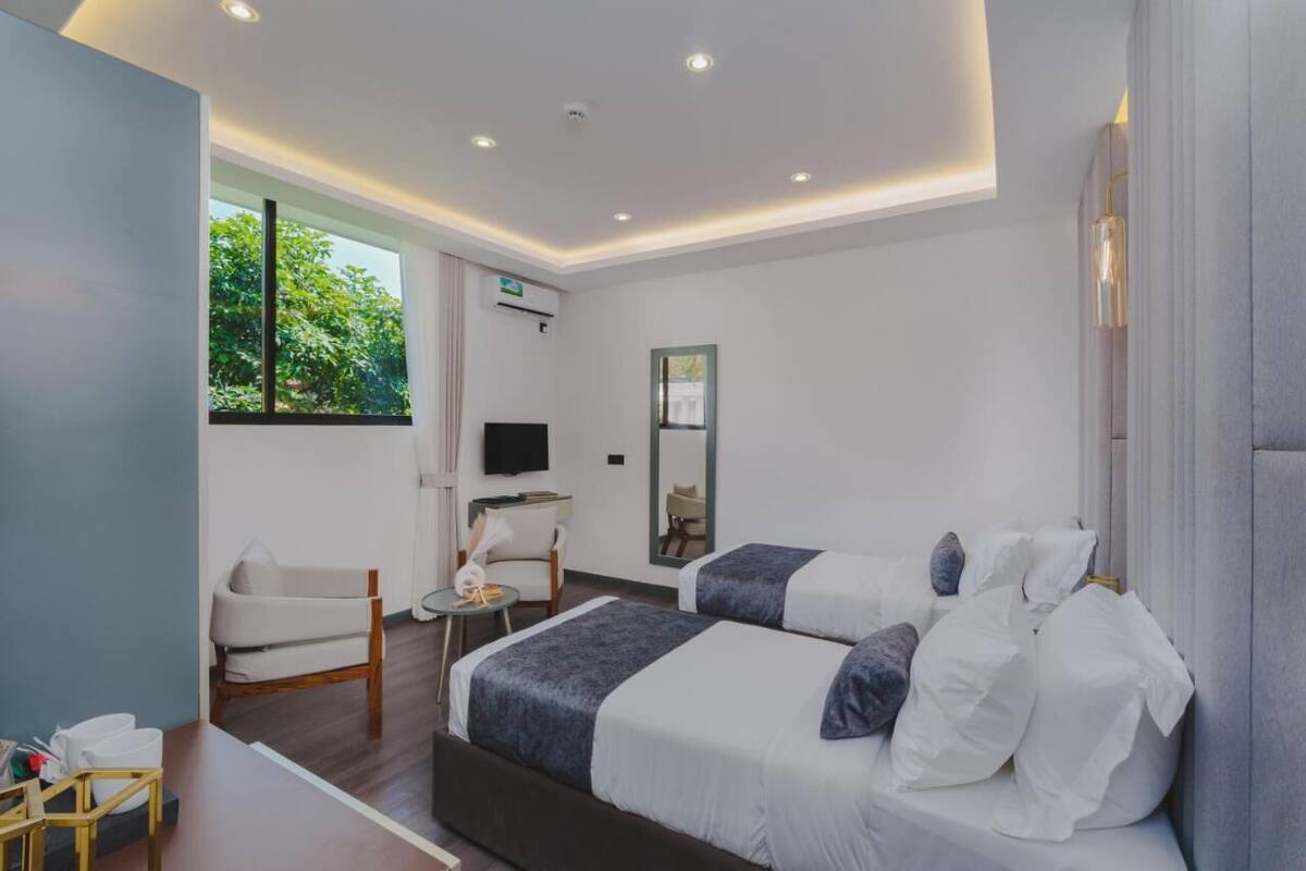 A modern hotel room with two beds, a desk, a chair, and a TV.