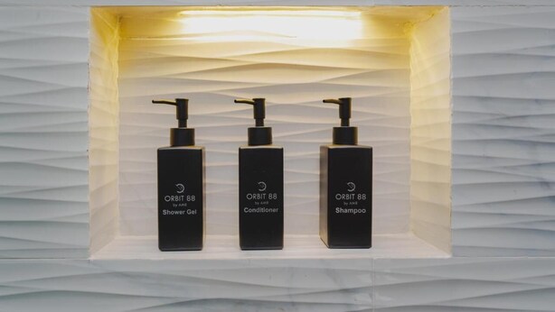 Three black bottles of AMR's ORBIT 88 products: shower gel, conditioner, and shampoo, in a white box with a textured background. - Orbit88 Hotel by AMR (Kandy)