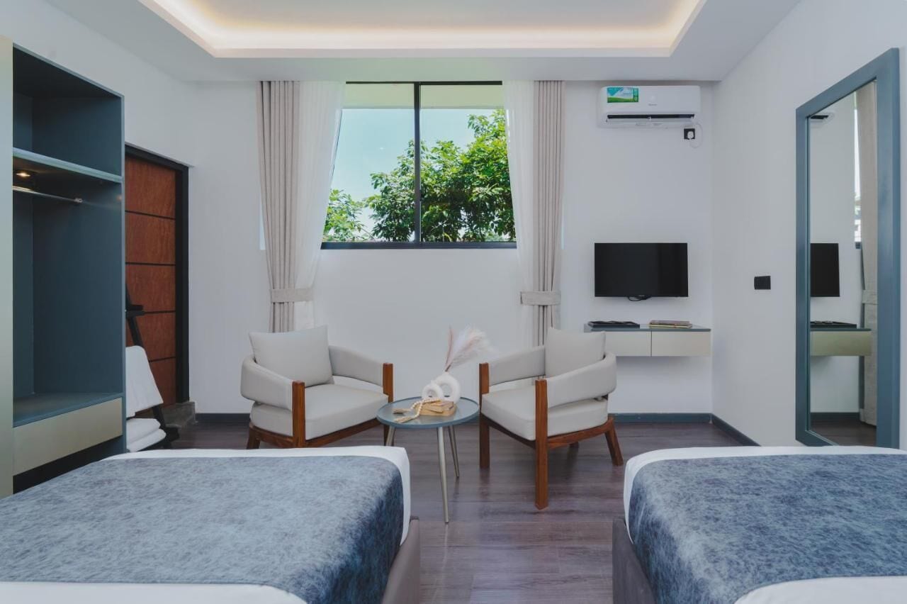 A hotel room with two beds, a TV, a small table with a decorative item, and a window with curtains.