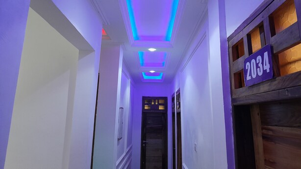Un pasillo con una puerta de madera identificada con el número 2034, techo con iluminación empotrada y tiras de LED azules.