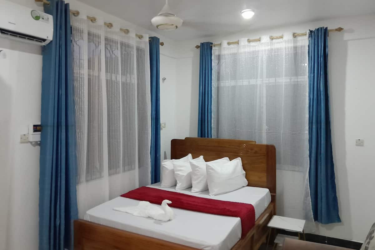 Una habitación de hotel con una cama, una manta roja, almohadas blancas y una decoración de cisne blanco.