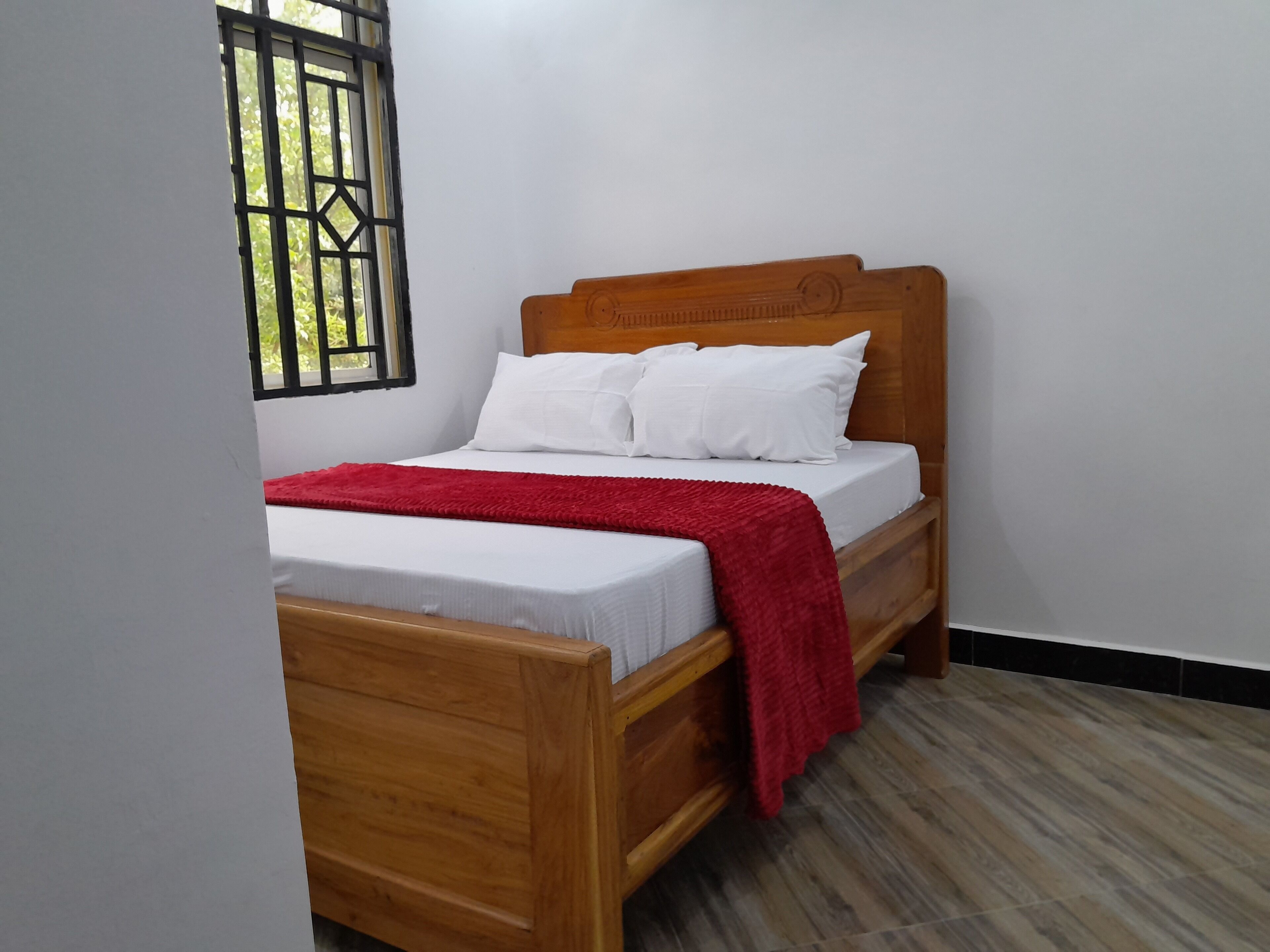 Una cama individual con cabecera de madera, ropa de cama blanca y una colcha roja.