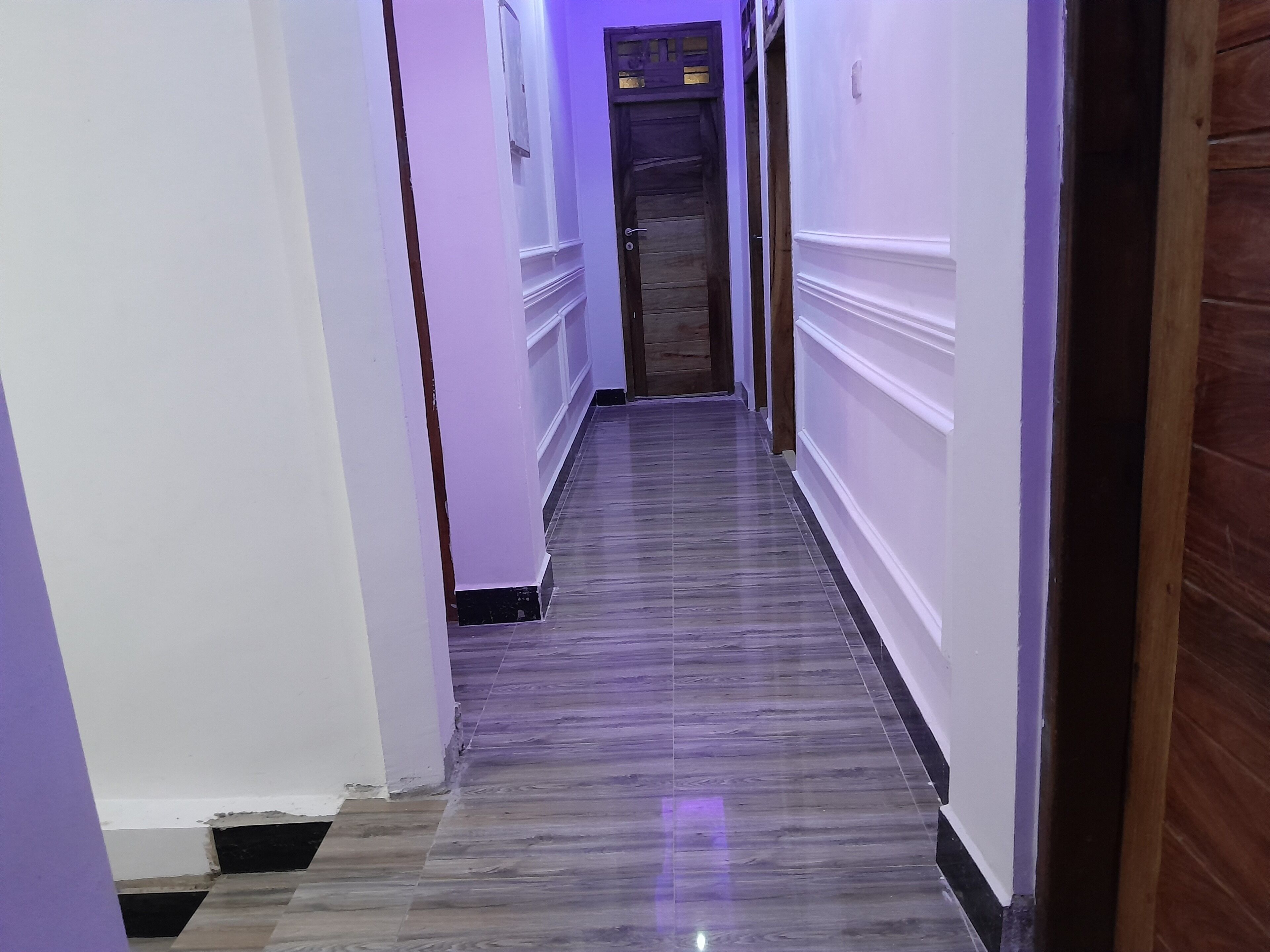 A narrow hallway with a wooden door at the end, white walls, and a tiled floor.