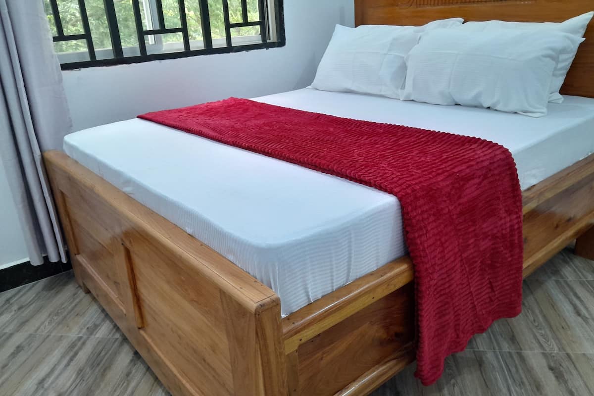 Una cama de madera con ropa de cama blanca y una manta roja.