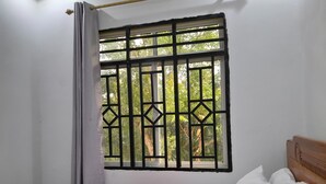 Una habitación con una cama, una ventana con reja metálica y vistas al exterior.
