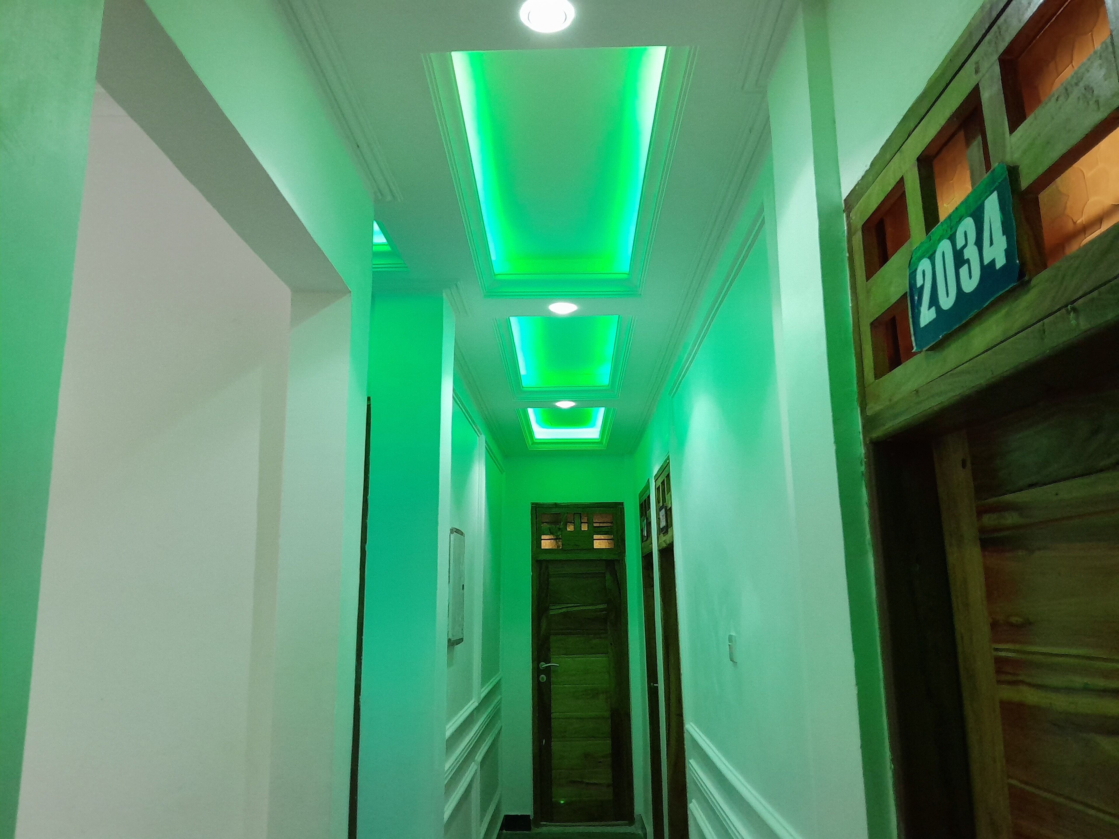A hallway with green lighting, a wooden door with the number 2034, and a traditional architectural style.
