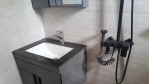 Un baño con lavamanos negro, un espejo encima y un cabezal de ducha de mano.
