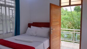 Una cama individual con ropa de cama blanca y una manta roja, una puerta de madera que da a un balcón con vistas a follaje.