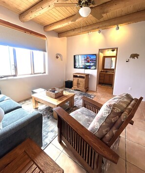 Una sala de estar con techo de madera, un televisor en la pared y una ventana con persianas.