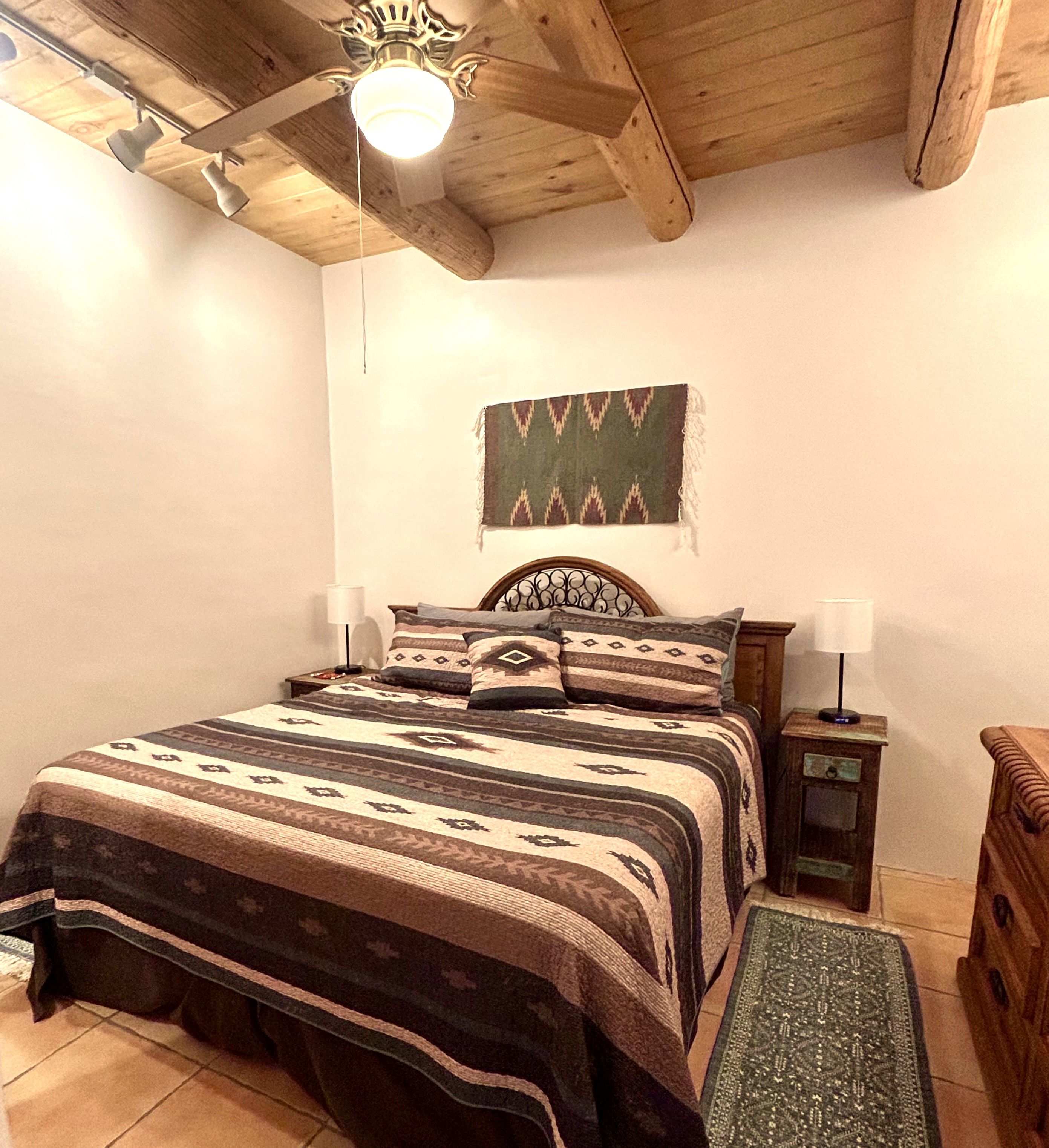 Une chambre avec un plafond en bois, un lit recouvert d’une literie à motifs, une œuvre d’art accrochée au mur et des lampes de chevet.