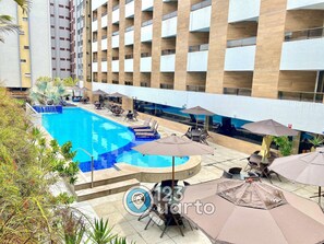 A swimming pool with lounge chairs and umbrellas, surrounded by a building with multiple floors and balconies. - Gold Flat Cabo Branco by 123Quarto Hospedagem (João Pessoa)