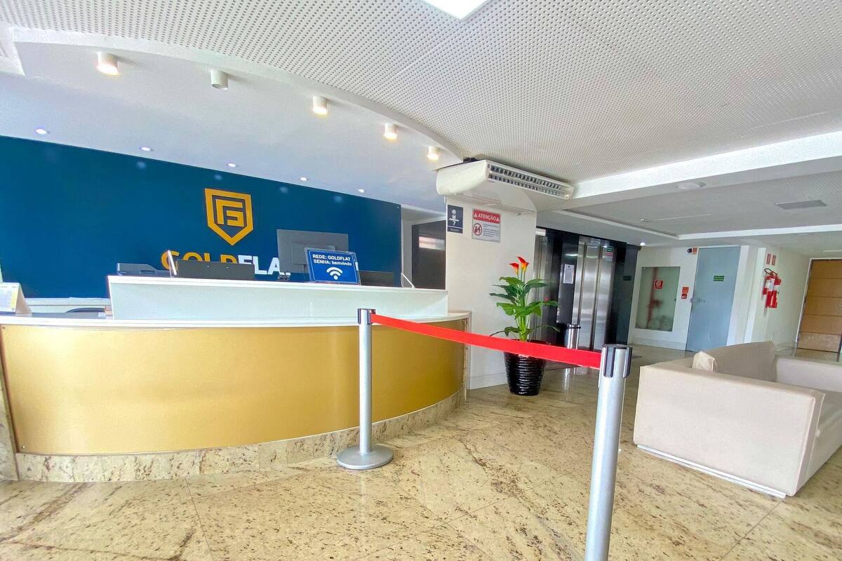 A reception area with a blue wall, a gold reception desk, a red rope barrier, a potted plant, and a sign indicating Wi-Fi availability.