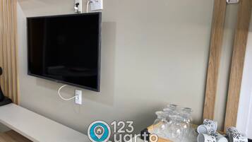 Quarto moderno com televisão na parede, prateleira de madeira com objetos decorativos e espelho.