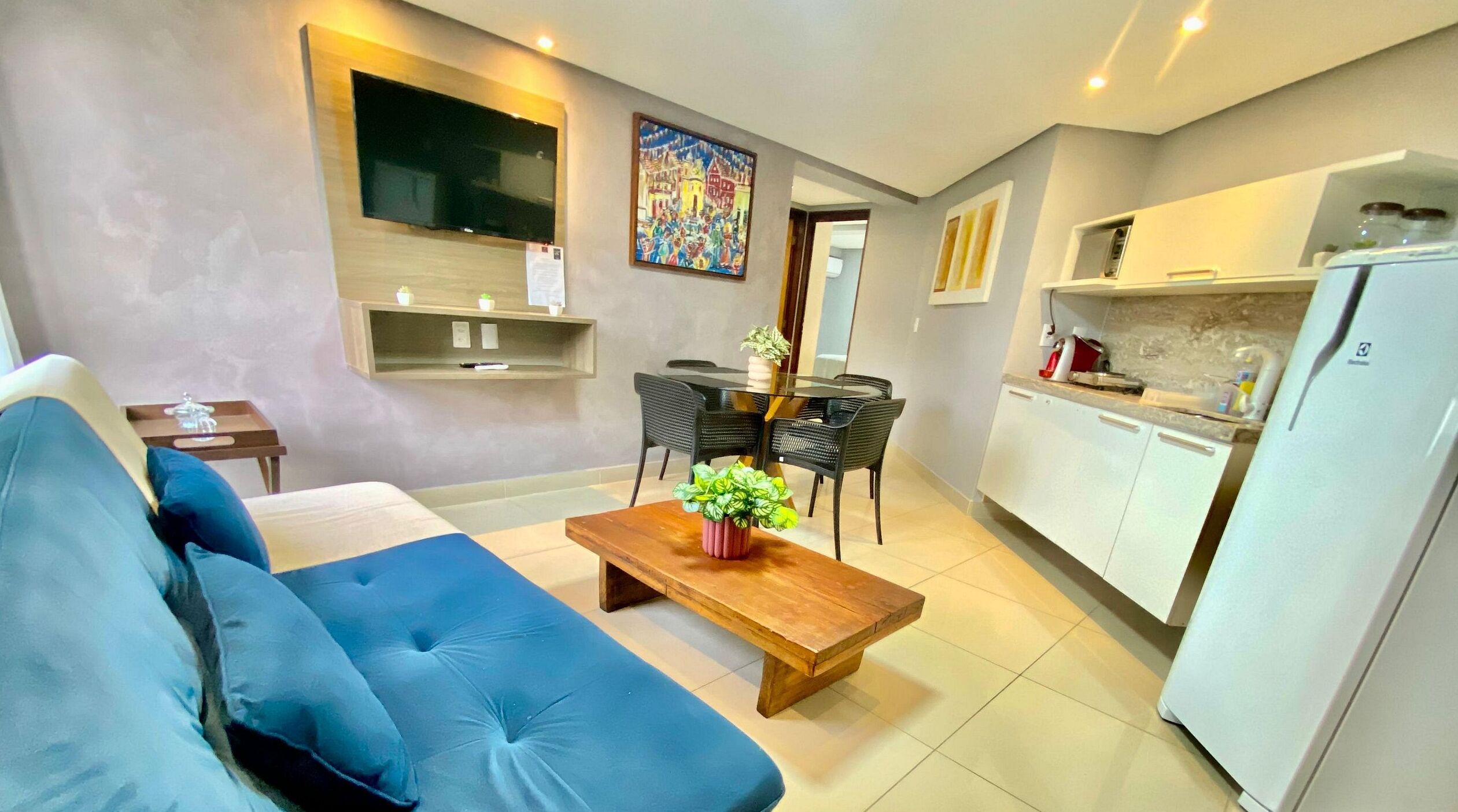 A modern living room with a blue sofa, a wooden coffee table, and a dining area with a glass table and black chairs.
