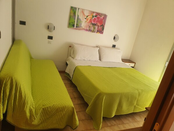 A room with two beds, each with a green bedspread, a white headboard, and a painting of flowers on the wall.