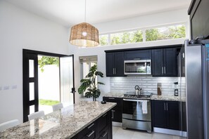 Une cuisine moderne avec des meubles de couleur sombre, un réfrigérateur en acier inoxydable, un four encastré et un grand îlot central doté d’un plan de travail en granit.
