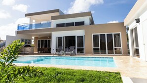 Ein modernes, zweistöckiges Haus mit Swimmingpool, großen Fenstern und einer überdachten Terrasse.