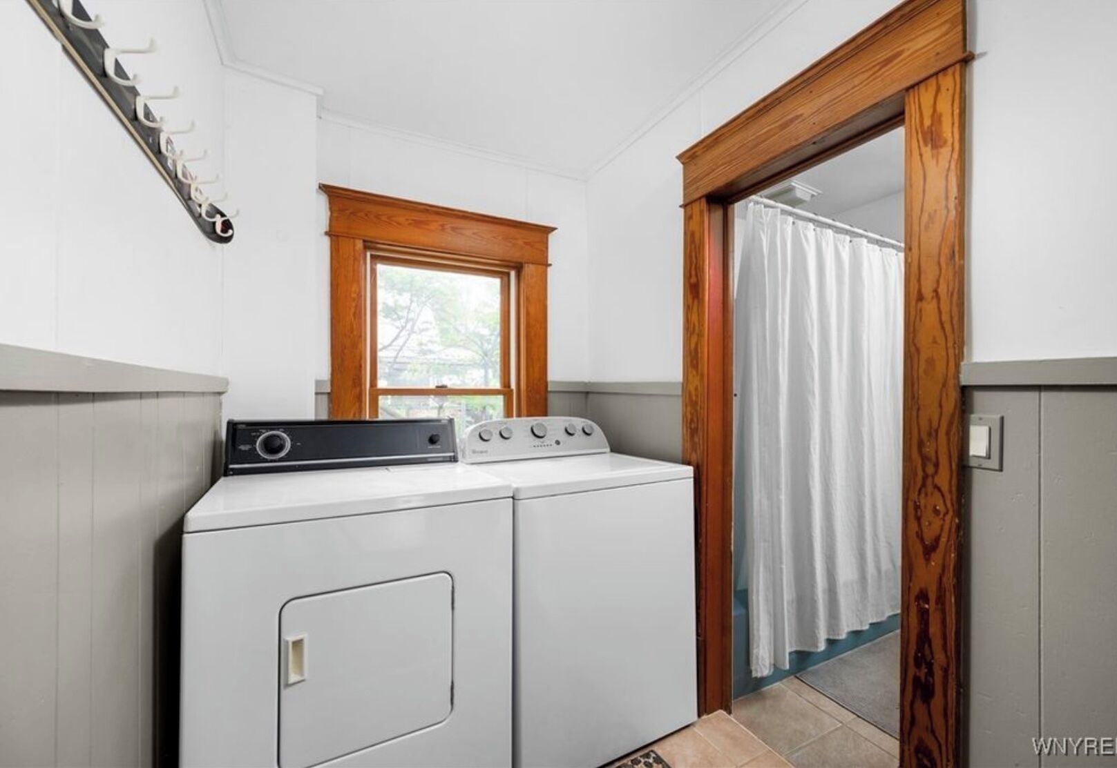 A compact laundry room with a washer and dryer, a wooden window, and a curtain-covered door.