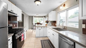 Una cocina moderna con armarios blancos, electrodomésticos de acero inoxidable y un amplio ventanal que proporciona luz natural.