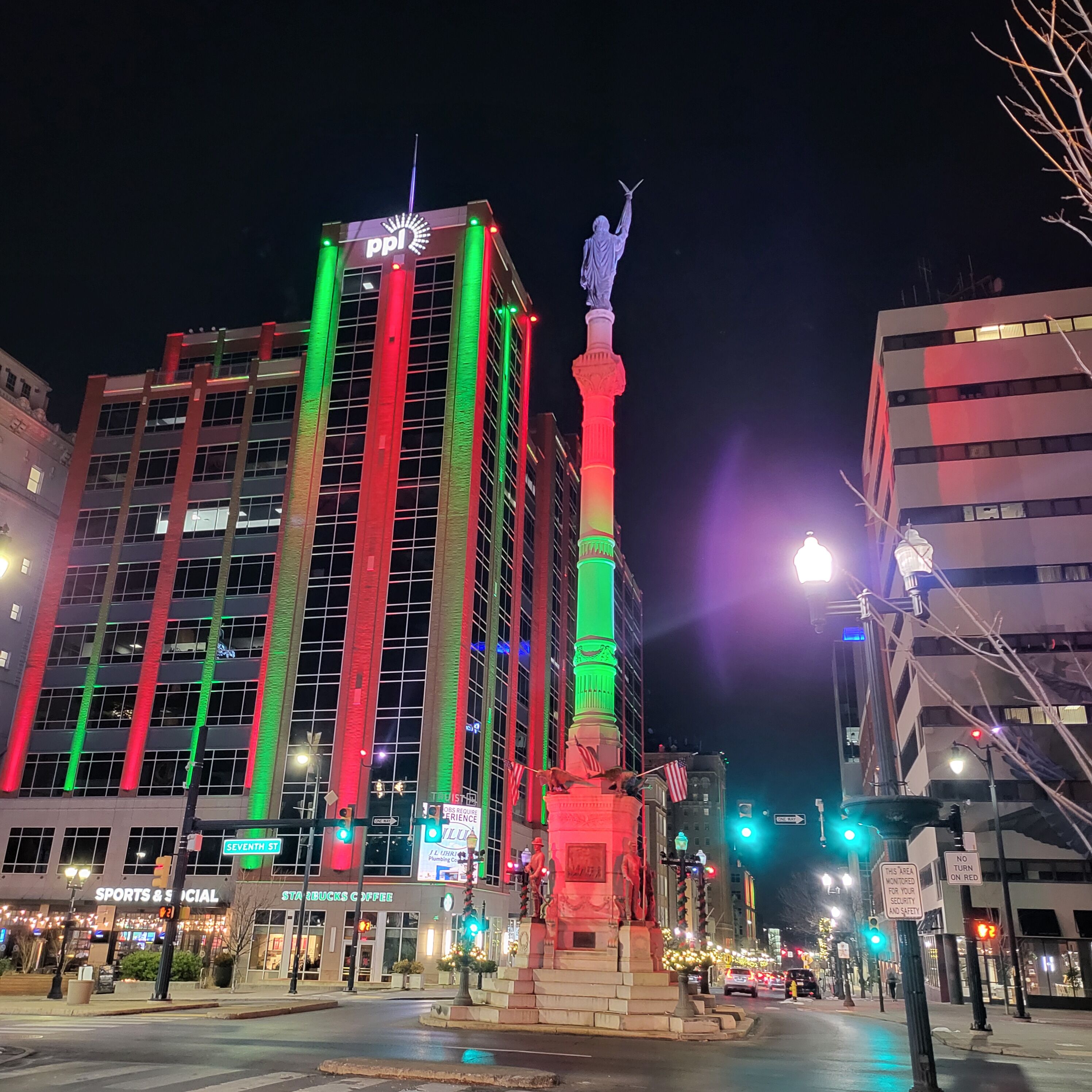 A brightly lit building with vertical stripes of red, green, and blue lights, a statue on a pedestal, and a Starbucks Coffee shop at the base.