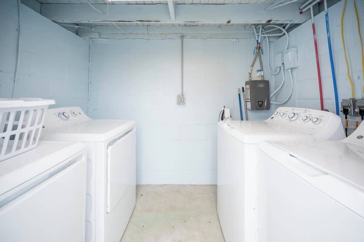 A laundry room with two white washing machines, a white laundry basket, and a water heater.