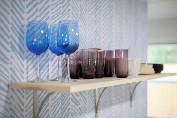 A shelf with various glassware, including two blue wine glasses and several tumblers.